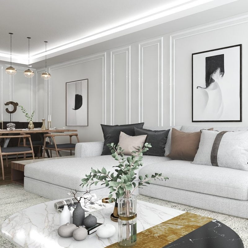 Açık gri modüler kanepe, mermer sehpa ve soyut duvar sanatına sahip modern bir oturma odası. Sarkıt lambalar, arka planda sandalyelerle ahşap bir yemek masasının üzerinde asılı duruyor ve bir iç mimarın sofistike dokunuşunu anımsatan bir atmosfer yaratıyor.
