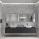 BANYO TASARIMI, mermer duvarlar, çift lavabo, büyük aynalar ve gri yüzen bir dolapla modern bir banyo sergiliyor. Ünlü bir iç mimar tarafından tasarlanan villa tarzı mekan, dolabın önündeki halıya sıcak bir ışık veren yumuşak bir aydınlatmaya sahip.